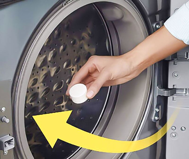 Hand placing a Splash Spotless tablet into the drum of a front-loading washer